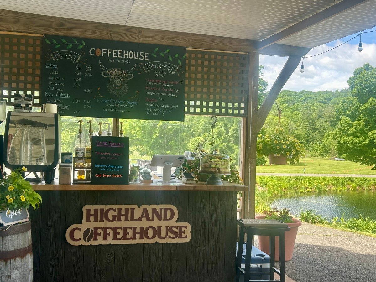 Highland Coffee House outdoor kiosk with green chalkboard menu, overlooking a pastoral landscape with trees and a pond